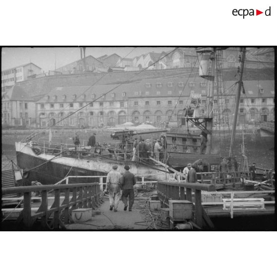 Dans le port de Brest, armement du chalutier Capitaine Armand, réquisitionné par la Marine nationale comme patrouilleur auxiliaire, au sein de la 4e escadrille de patrouilleurs auxiliaires (EPA) de la 2e région maritime (RM).