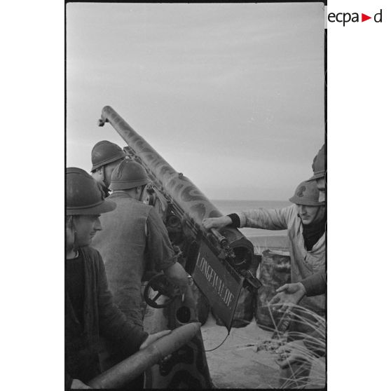 Chargement par des canonniers d'un canon de 75 mm antiaérien camouflé, baptisé Longewalde, affecté à une batterie d'artillerie de défense côtière de la Marine nationale sur le littoral.