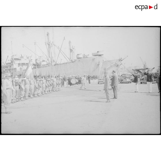 Les autorités militaires saluent le drapeau du 1er régiment de tirailleurs algériens (1er RTA) sur un quai du port d'Alger.