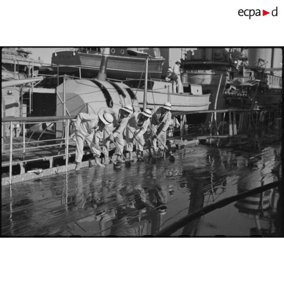 Des marins briquent le pont du croiseur lourd Duquesne.