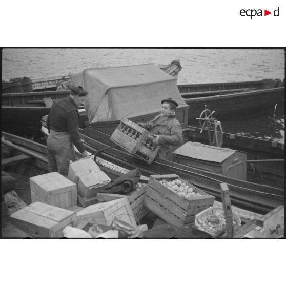 Des marins, de corvée de vivres, embarquent dans des chaloupes le ravitaillement destiné à une escadre qui mouille au large.