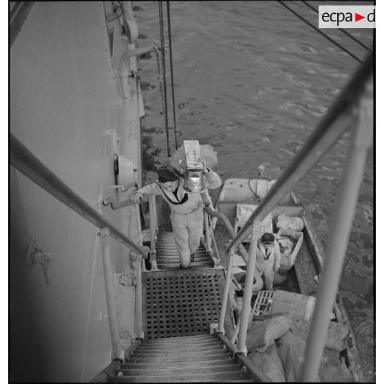 Déchargement de caisses de vivres par une échelle de coupée à bord d'un navire au mouillage dans la rade de Brest.<br>Cette photographie est en fait la photographie MARINE 101-1081.