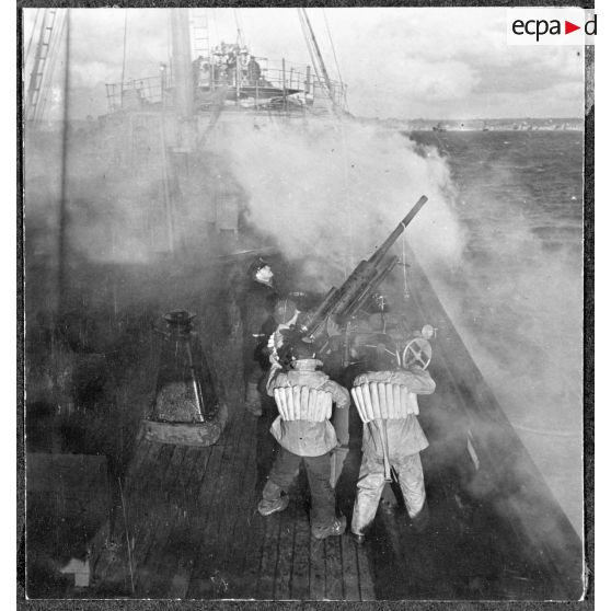 Des canonniers ouvrent le feu sur un objectif avec un canon antiaérien de 37 mm à bord d'un cargo naviguant en convoi, réquisitionné et armé par la Marine nationale.
