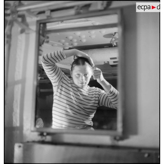 Un marin se coiffe dans les locaux communs réservés aux hommes d'équipage à bord du croiseur (ou cuirassé) Dunkerque.