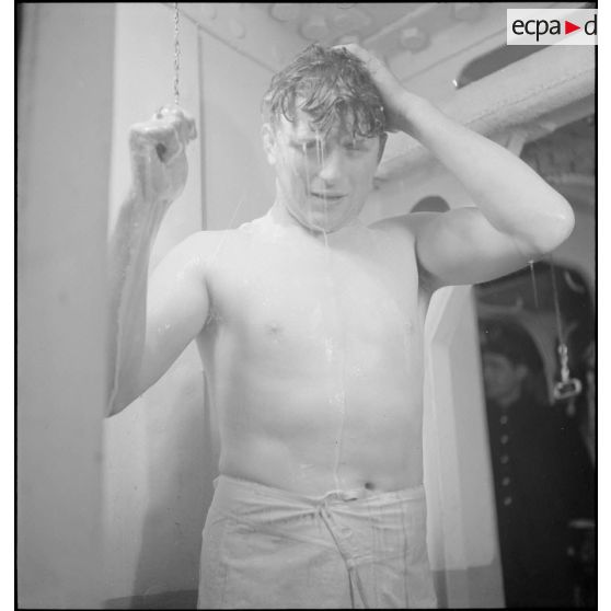 Un marin prend une douche dans les locaux communs réservés aux hommes d'équipage à bord du croiseur (ou cuirassé) Dunkerque.