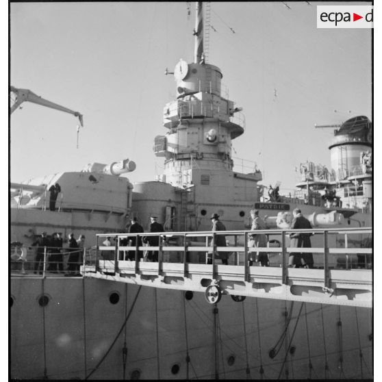 Des journalistes américains en visite à Brest montent à bord du cuirassé Dunkerque par une échelle de coupée.