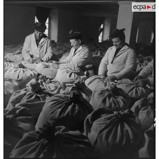 Des marins ficellent des sacs de farine entreposés dans un magasin de l'intendance à Brest.