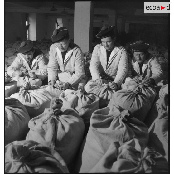 Des marins ficellent des sacs de farine entreposés dans un magasin de l'intendance à Brest.