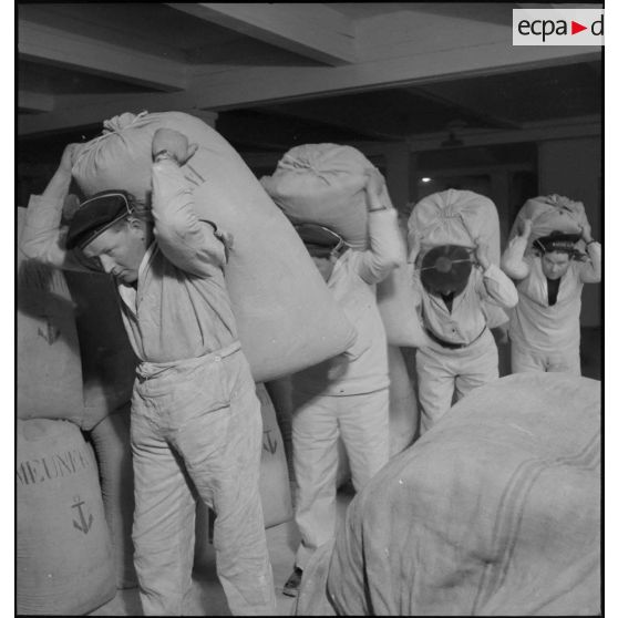 Des marins minotiers entreposent ou transportent des sacs de farine dans un magasin de l'intendance à Brest.