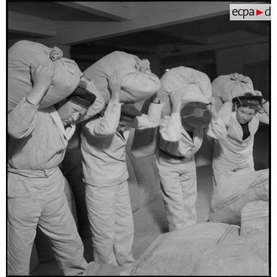 Des marins minotiers entreposent ou transportent des sacs de farine dans un magasin de l'intendance à Brest.