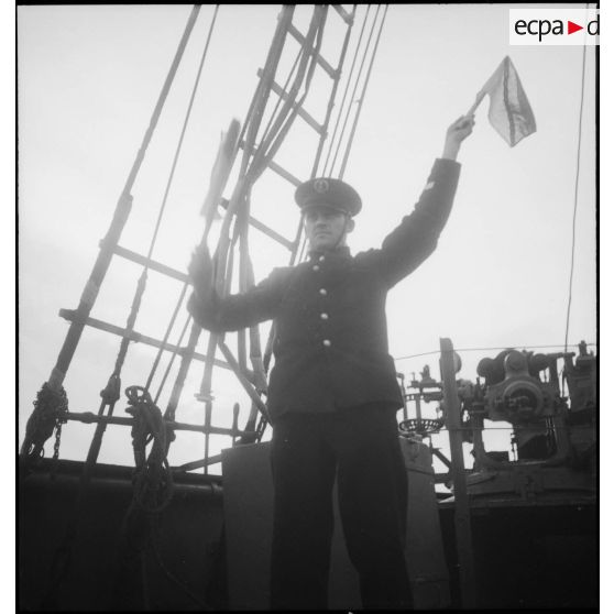 Un second maîre actionne des signaux à bras à bord du chalutier Patrie, réquisitionné par la Marine nationale et armé en patrouilleur auxiliaire, à destination d'un autre navire.