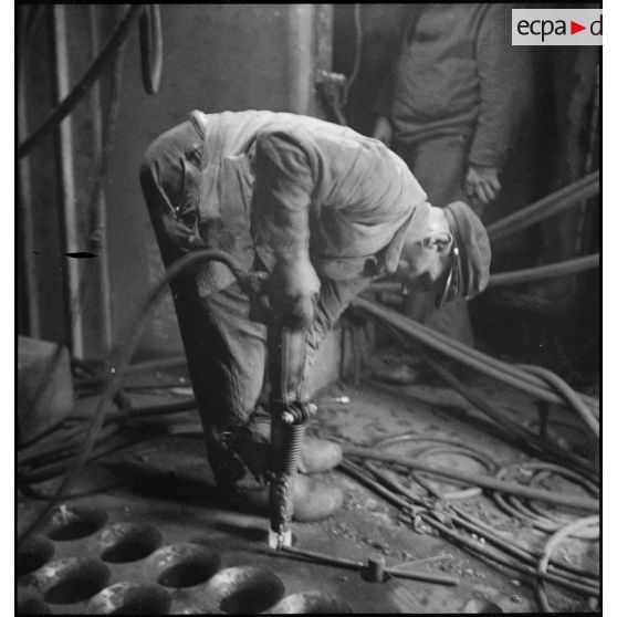 Un ouvrier fixe des rivets à bord du cuirassé Richelieu en cours d'achèvement dans l'arsenal de Brest.