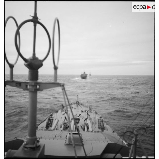 Convoi de navires transports de troupes naviguant en ligne de file vers la France, escortés par des bâtiments de la Marine nationale.
