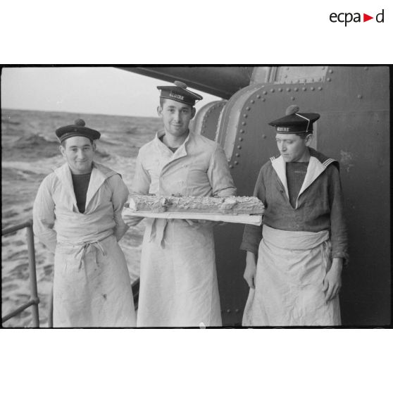 Les marins cuisiniers présentent la bûche du repas de réveillon du Nouvel An à bord du croiseur la Gloire.