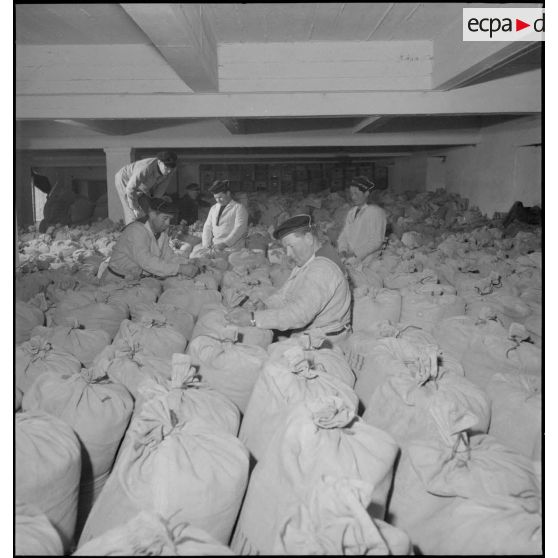 Des marins ficellent des sacs de farine entreposés dans un magasin de l'intendance à Brest.