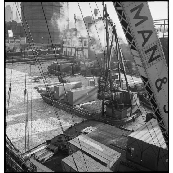 Dans le port de New-York pris par les glaces, des chalands transportent des caisses contenant des avions destinés aux Alliés, qui vont être chargées sur des cargos.