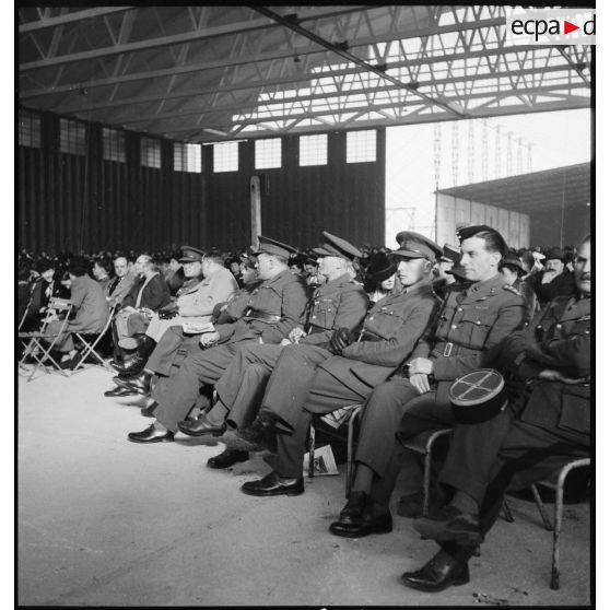Officiers britanniques et français assistant au tirage de la tranche de la Marine de la loterie nationale dans un hangar de la base d'aéronautique navale de Cherbourg.