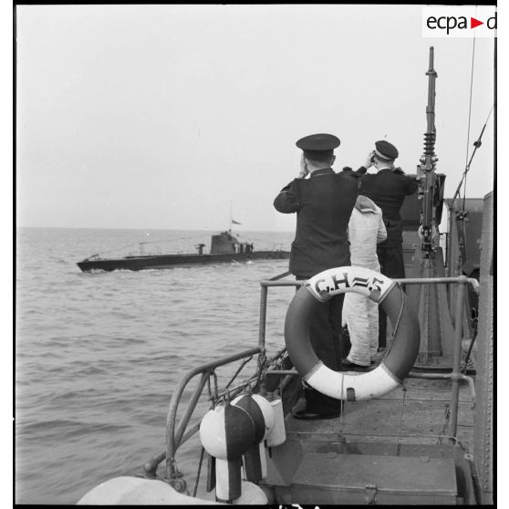 Un officier et un officier marinier, à bord du chasseur de sous-marins n°5, observent l'un d'entre eux naviguant sur leur bord.