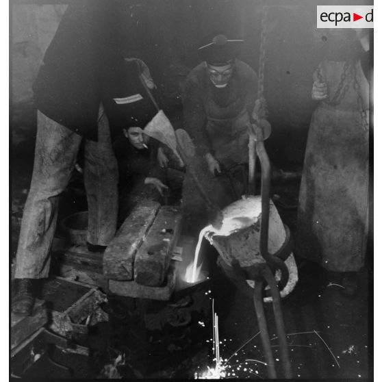 Atelier central de la flotte : des marins fondent une pièce de métal.