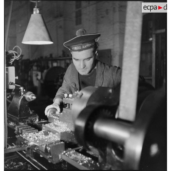 Atelier central de la flotte : un marin travaille une pièce de métal sur un tour.