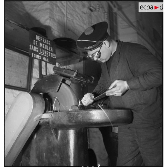 Atelier central de la flotte : un marin travaille une pièce de métal avec une meule.