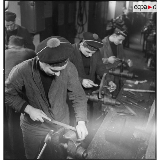 Atelier central de la flotte : des marins liment des pièces de métal.