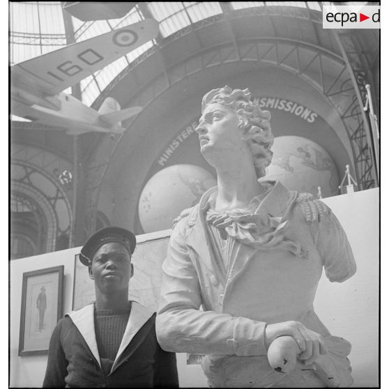 Exposition de la France d'Outre-mer au Grand Palais : marin originaire des colonies posant à côté du moulage de la figure de proue d'un navire.