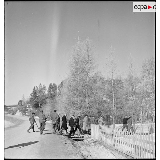 Des civils norvégiens et des soldats français circulent à pied sur une route.