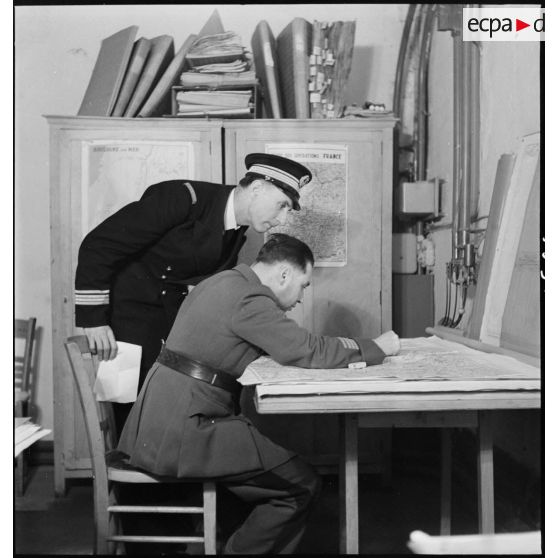 Un capitaine de corvette et un commandant français sont penchés sur une carte au poste de commandement de l'amiral Abrial à Dunkerque.