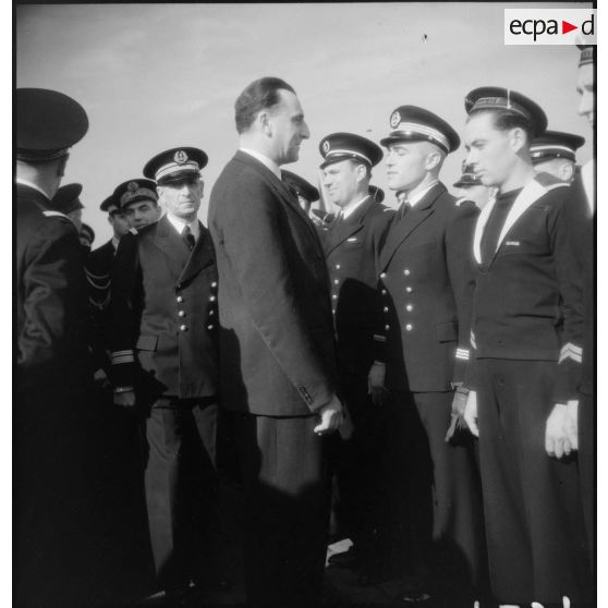 Louis Jacquinot, ministre de la Marine, passe en revue des officiers, officiers mariniers et marins lors d'une cérémonie à bord d'un bâtiment.