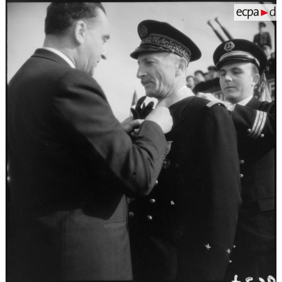 Louis Jacquinot, ministre de la Marine, remet l'insigne de commandeur de la Légion d'honneur à un contre-amiral lors d'une cérémonie à bord d'un bâtiment.