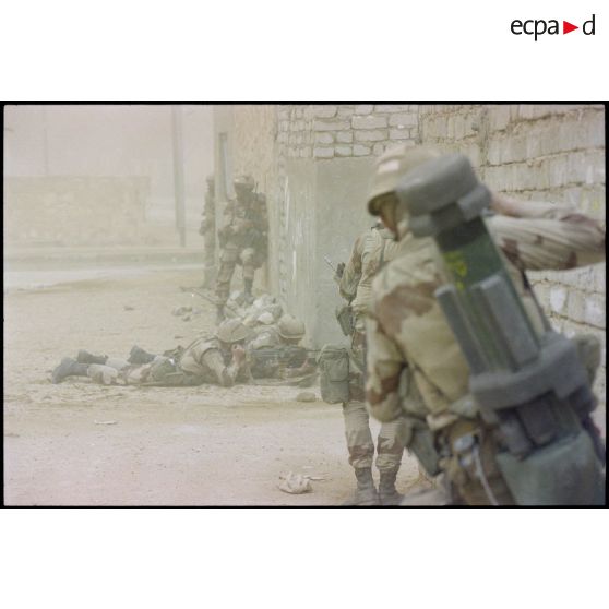 Des marsouins du 3e RIMa (régiment d'infanterie de marine) investissent la ville d'Al Salman, postés à l'angle d'une rue. Ils ne portent pas de S-3P (survêtement de protection à port permanent) NBC (risque nucléaire, bactériologique et chimique). Un Apilas est visible dans le dos d'un marsouin.