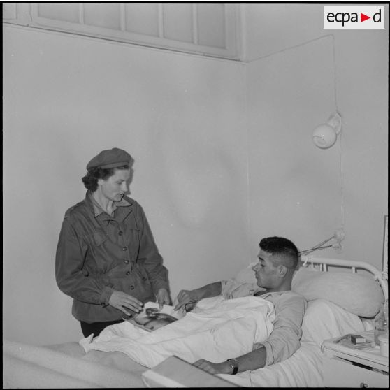 Mlle Lilia, infirmière-PFAT, au chevet d'un blessé convalescent.