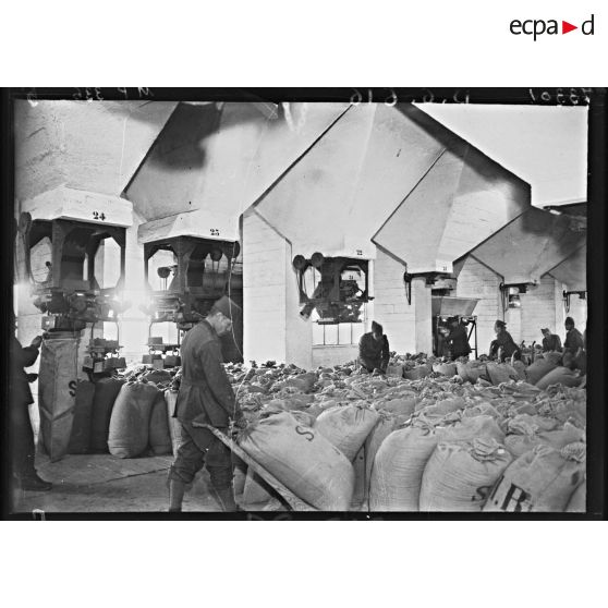 Sous des silos à grains des soldast manipulent des sacs de farine.