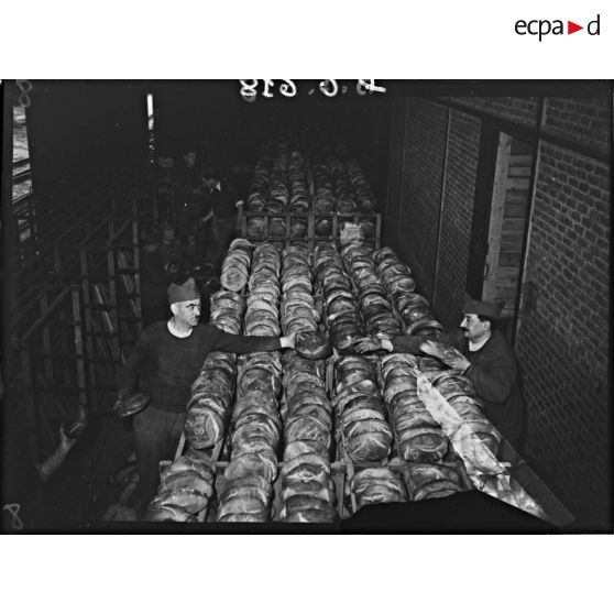 Des soldats rangent des boules de pains dans de vastes paniers métalliques.