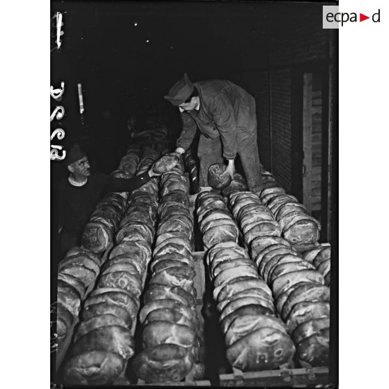 Des soldats rangent des boules de pains dans de vastes paniers métalliques.