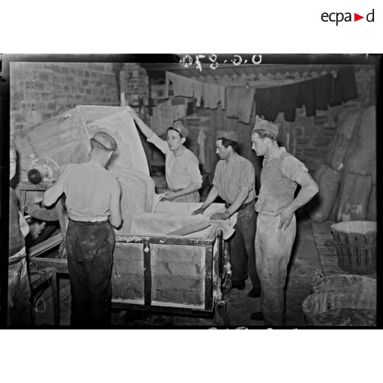 Des boulangers versent la pâte à pain dans des chariots de bois.