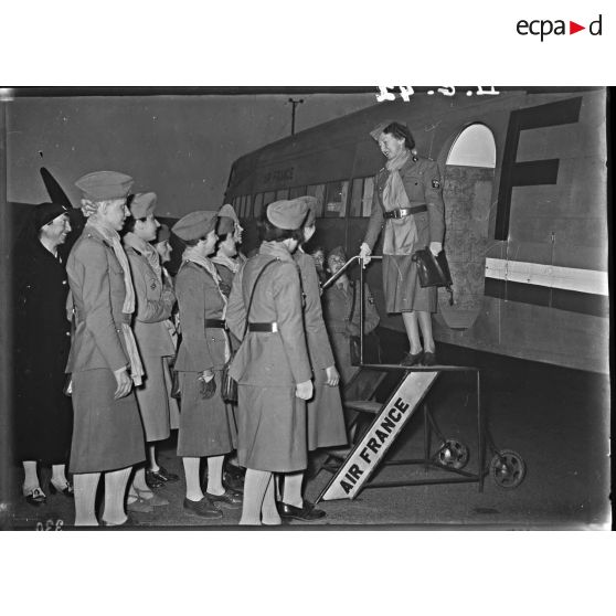 Madame Paul Reynaud du haut de la passerelle de l'avion d'air France salue les conductrices de la section sanitaire.