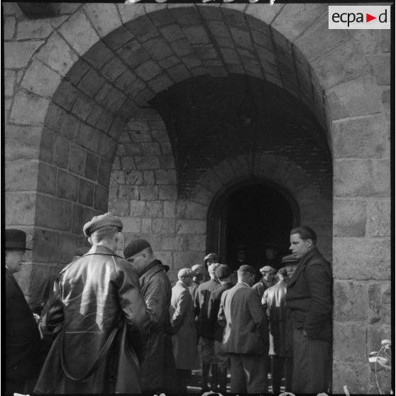 Plan général d'hommes qui attendent de passer en conseil de révision sous un porche.