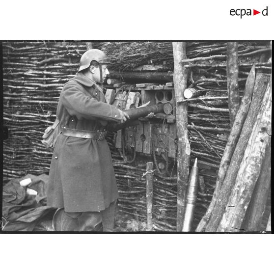 Un soldat range un obus de 75 mm dans un logement prévu à cet effet dans un muret en bois.