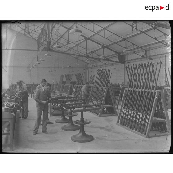 Plan général d'un atelier d'une usine d'armement où des ouvriers travaillent au montage de canons.