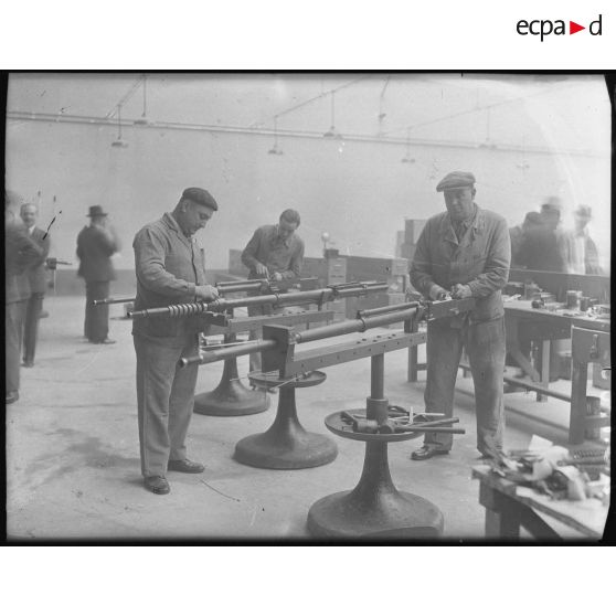 Plan général d'un atelier d'une usine d'armement où des ouvriers travaillent au montage de canons.