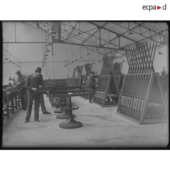 Plan général d'un atelier d'une usine d'armement où des ouvriers travaillent au montage de canons.