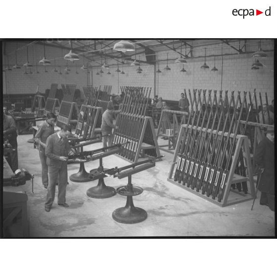 Plan général d'un atelier d'une usine d'armement où des ouvriers travaillent au montage de canons.