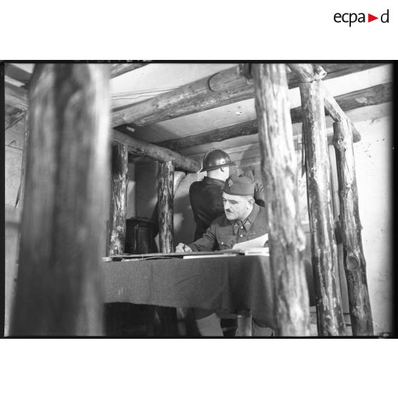 Plan général de l'intérieur d'un poste de commandement, des sous-officiers attablés travaillent.