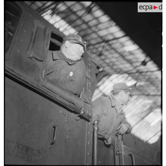 Plan moyen du chauffeur et du mécanicien qui se penchent à la fenêtre de leur locomotive.
