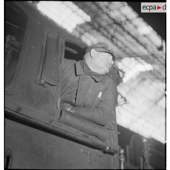 Plan moyen du chauffeur et du mécanicien qui se penchent à la fenêtre de leur locomotive.