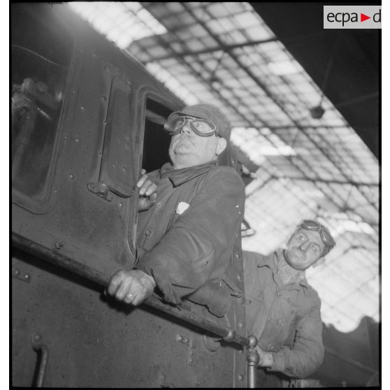 Plan moyen du chauffeur et du mécanicien qui se penchent à la fenêtre de leur locomotive.