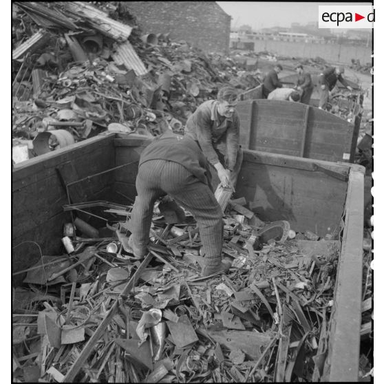 Deux ouvriers effectuent un tri dans l'entassement de ferraille à l'extérieur de l'usine.
