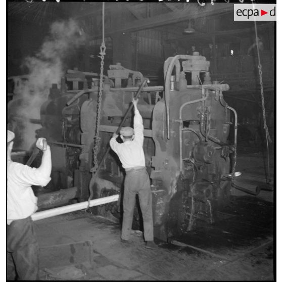 A l'intérieur de l'usine des ouvriers passent au laminage une pièce métallique chauffée à blanc.